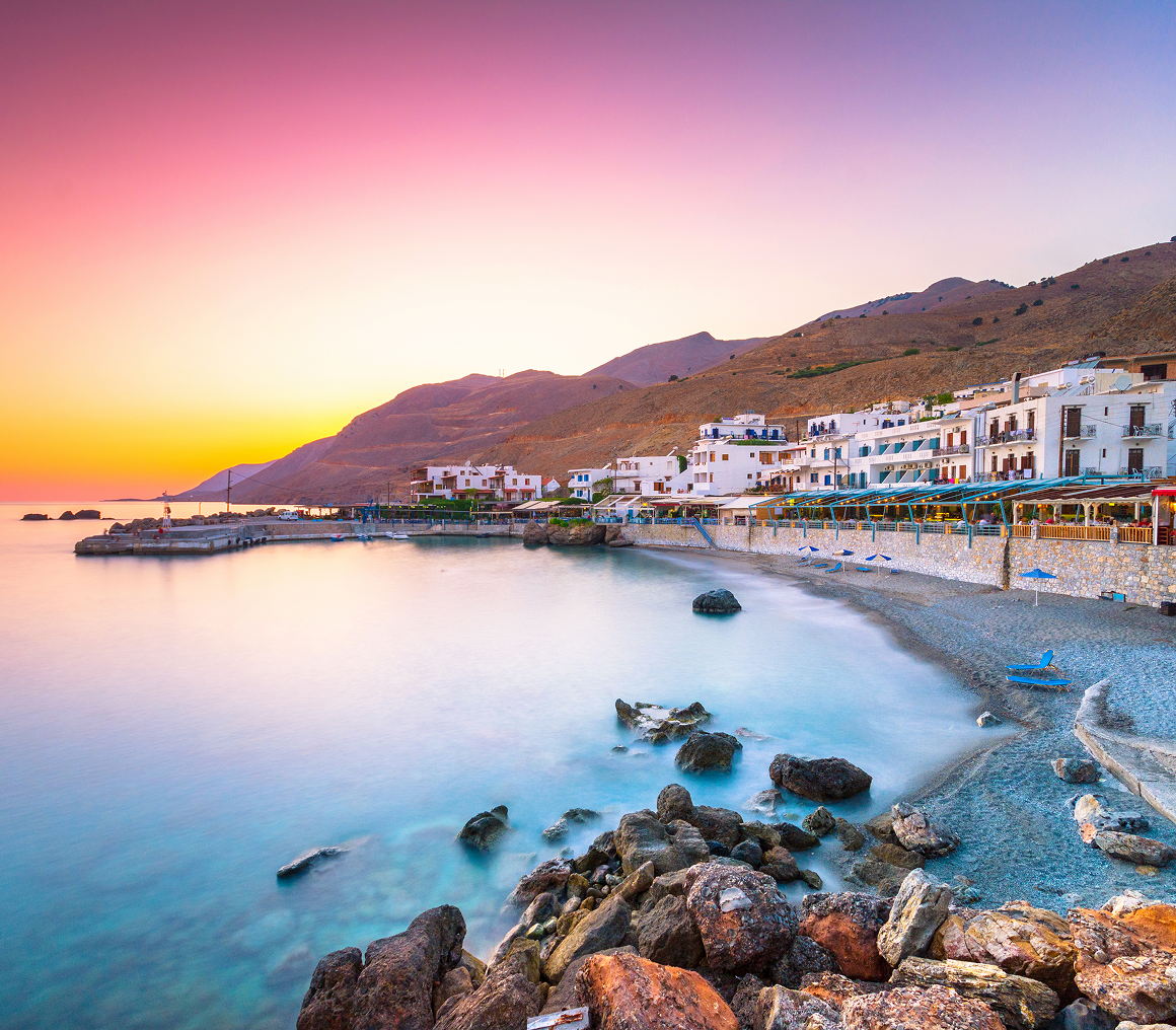 Seaside village at sunset with colorful sky.